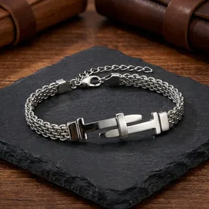 Detail shot of masculine stainless steel mesh woven bracelet with buckle charm on slate.