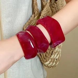 Close-up of irregular red marbled resin bangles worn on a model's arm with a straw bag
