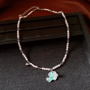 Vue détaillée d'un pendentif chiot vert sur un collier de perles blanches et claires.