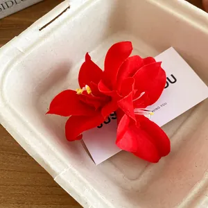 Detailed close-up of a vibrant red hibiscus fabric flower hair clip in a beige gift box