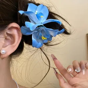 Detail view of a blue fabric flower hair clip on dark hair for seaside vacation style.
