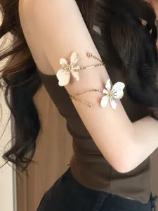 Detail eines eleganten goldfarbenen Oberarmreifs mit weißen Emaille-Blumen am Arm