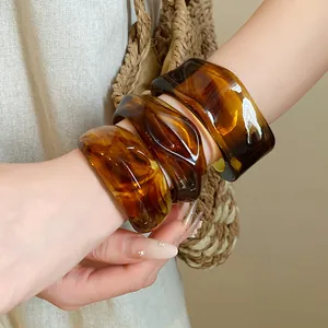 Detailed view of irregular geometric marbled amber resin open bangles worn on wrist
