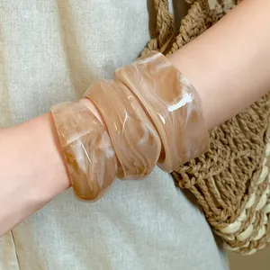 Close-up of three irregular marbled acrylic chunky bangles worn on a model's arm with straw bag