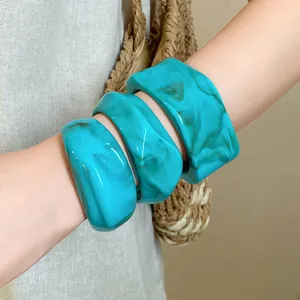 Close-up of irregular turquoise marbled bangles styled on a wrist with a woven bag.