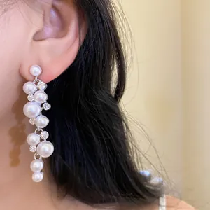 Detailed macro view of elegant white pearl and rhinestone tassel earrings on model ear