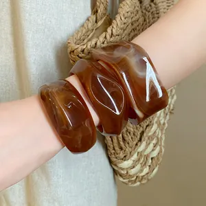 Detailed macro view of irregular geometric amber marbled resin bangles worn on arm.