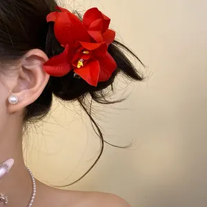 Macro detail of a vibrant red fabric flower hair clip elegantly worn on model's dark hair.