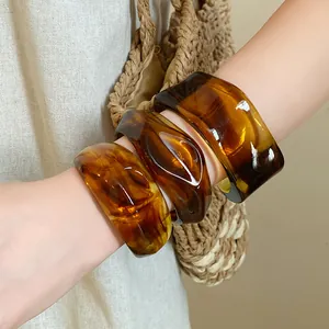 Close-up of irregular geometric marbled resin open bangles with amber texture worn on wrist