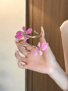 Nahaufnahme eines goldenen Armreifs mit zwei zarten rosa Emaille-Blumen in der Hand