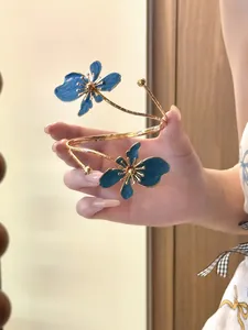 Detailansicht einer goldfarbenen Armspange mit zwei exquisiten blauen Emaille-Blumen.