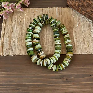 Retro ethnic style shell bead necklace with green and white circular discs on a mat.