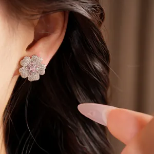 Detail view of an elegant flower stud earring with pink and clear zircons worn on the ear