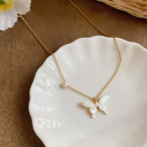 Macro view of dainty gold necklace with iridescent butterfly and pearl detail on a white shell.