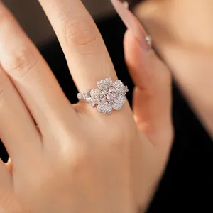 Close-up view of an elegant silver flower ring featuring pink and white zircons on a model hand