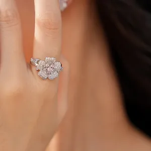 Macro view of an elegant silver flower ring pavé-set with pink and white zircons on a finger.