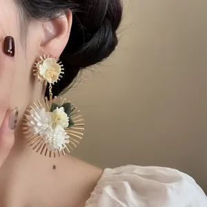 Elegantes pendientes de flores de tela con marco dorado de rayos de sol