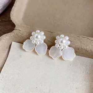 Elegantes pendientes de flores de perlas con pétalos blancos sobre fondo de textura natural.