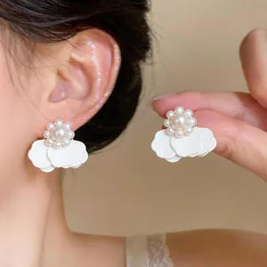 Primer plano de elegantes pendientes de flores blancas y perlas usados y sostenidos