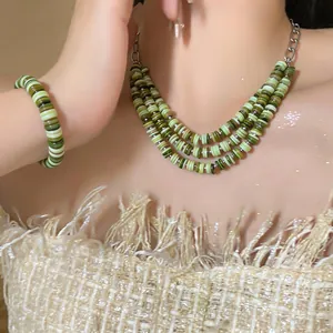 Close-up of bohemian three-layer green shell bead necklace and matching bracelet set on model.