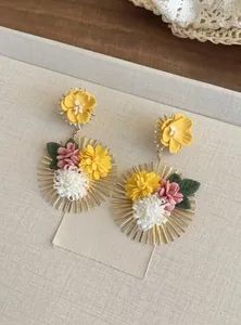 Detalle de pendientes colgantes de flores de tela hechos a mano con diseño de sol dorado.