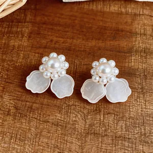 Detalle de elegantes pendientes de perlas con forma de flor blanca sobre fondo de madera