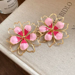 Close-up detail of vintage pink enamel flower earrings with gold-toned outlines on a book.