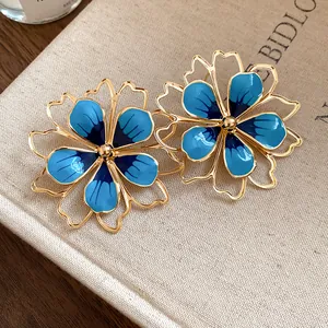 Close-up detail of vintage blue enamel flower jewelry set on a textured beige book cover.