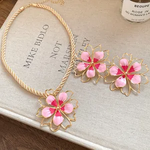Close-up of pink enamel flower pendant necklace and earrings with gold rope chain.