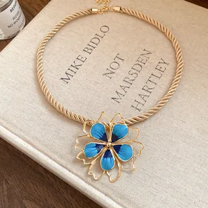 Detailed view of a vintage gold rope necklace with a large blue enamel flower pendant.