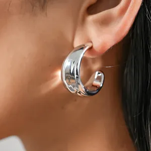 Detailed macro shot of a chunky silver C-shaped geometric hoop earring worn on model's ear