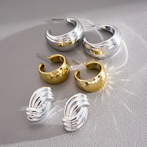 Macro view of geometric C-shaped and ribbed silver and gold earrings with mixed textures.