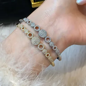 Primer plano de brazaletes geométricos de circón en oro y plata en la muñeca.