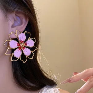 Close-up of an oversized pink enamel flower earring with gold hollow outlines