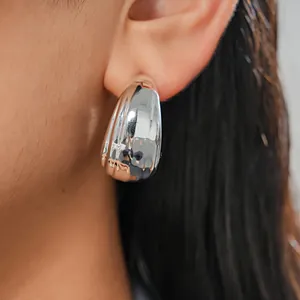 Macro detail of a minimalist silver chunky C-shaped geometric hoop earring worn on an ear