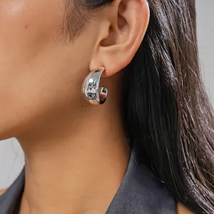 Detailed side view of a polished silver C-shaped geometric earring on a model's ear