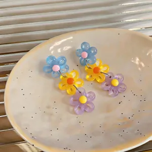 Detailed close-up of colorful daisy drop earrings in light blue, yellow, and purple.