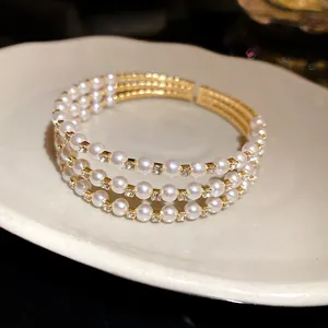 Close-up view of elegant three-layer gold bangle with white pearls and sparkling crystals.
