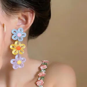 Close-up view of colorful acrylic daisy drop earrings on an Asian model's ear