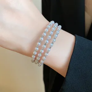 Close-up detail showing an elegant three-layer pearl bracelet with rhinestone accents.