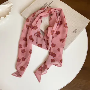 Detailed close-up of a vintage pink chiffon scarf with brown floral prints on a white table.