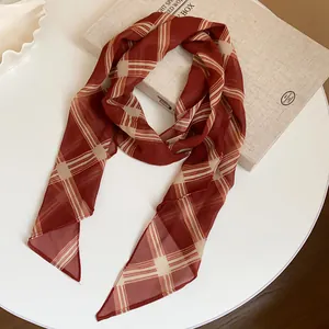 Detail shot of elegant red and white plaid chiffon scarf displayed on a cream book