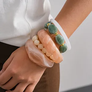Close-up of layered acrylic bangles and beaded bracelets in marble peach and green.