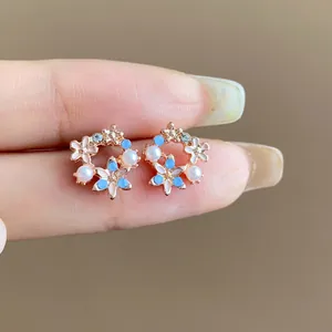 Dettaglio ravvicinato di orecchini a lobo floreali oro rosa con perle e accenti blu