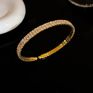Primer plano de un elegante brazalete abierto dorado con dos filas de cristales brillantes.