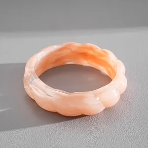 Close-up of a peach marbled acrylic bangle with a unique wavy geometric edge design.
