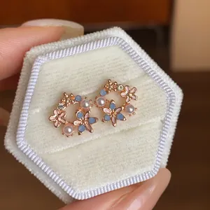 Vista dettagliata di eleganti orecchini a lobo con fiori e perle in oro rosa su velluto.