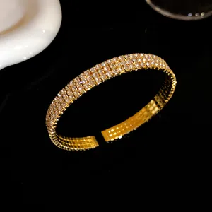 Primer plano de un elegante brazalete abierto dorado con tres filas de cristales brillantes.