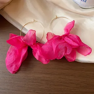 Detail view of vibrant magenta fabric flower hoop earrings presented on soft silk fabric