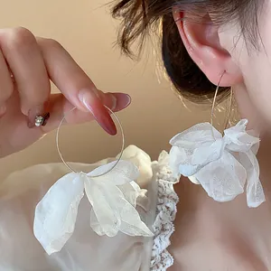 Detailed close-up showing the delicate white fabric flower on gold-tone hoop earrings